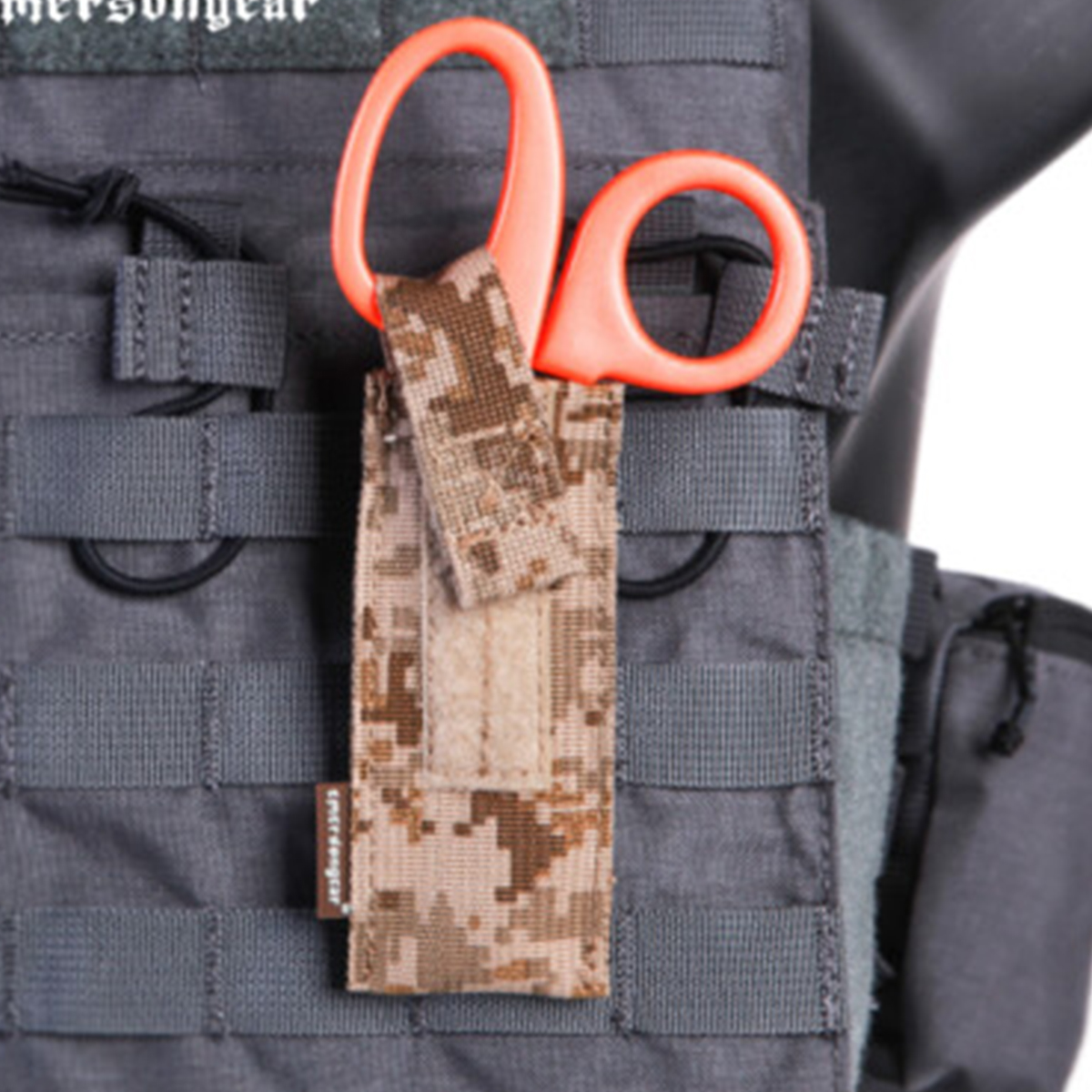 Trauma shears secured in a camouflage pouch attached to a gray tactical vest